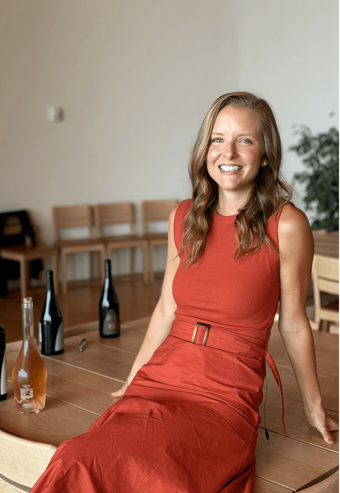 A young caucasian woman in a red dress smiles and leans back against a table